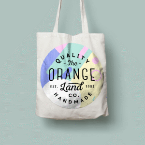 White tote bag with a pastel circular logo containing the text 'Quality The Orange Land Co. Handmade' and 'Est. 1982'